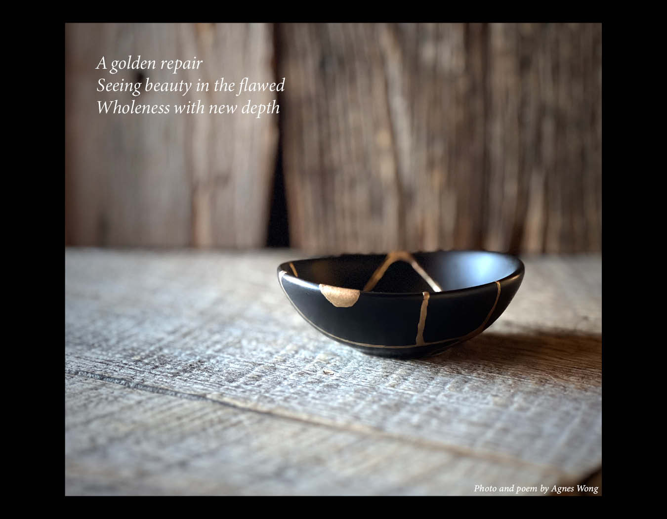 A black ceramic bowl repaired with golden seams rests on a rustic wooden table.