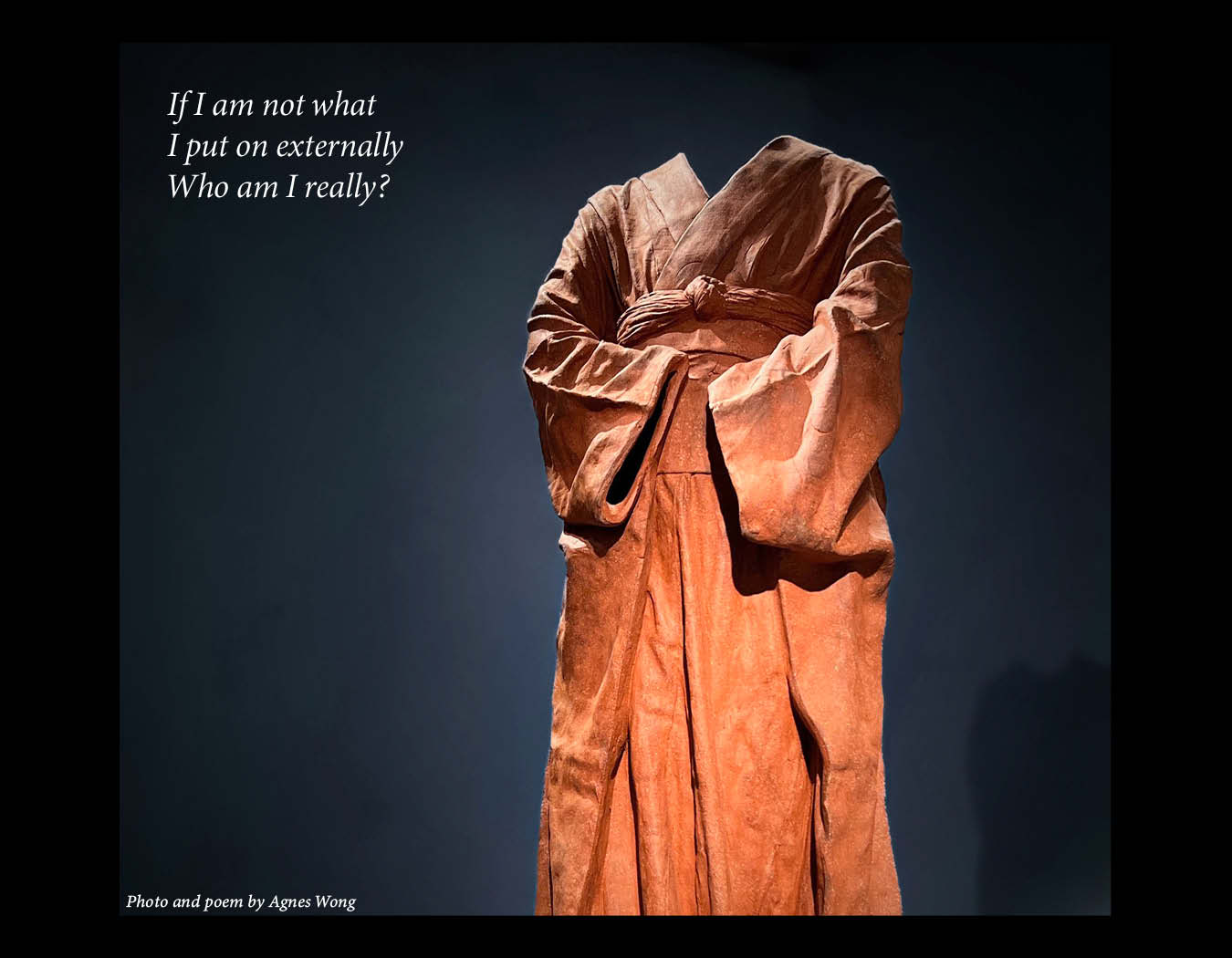 A headless terracotta-coloured robed sculpture with folded arms stands against a dark background.